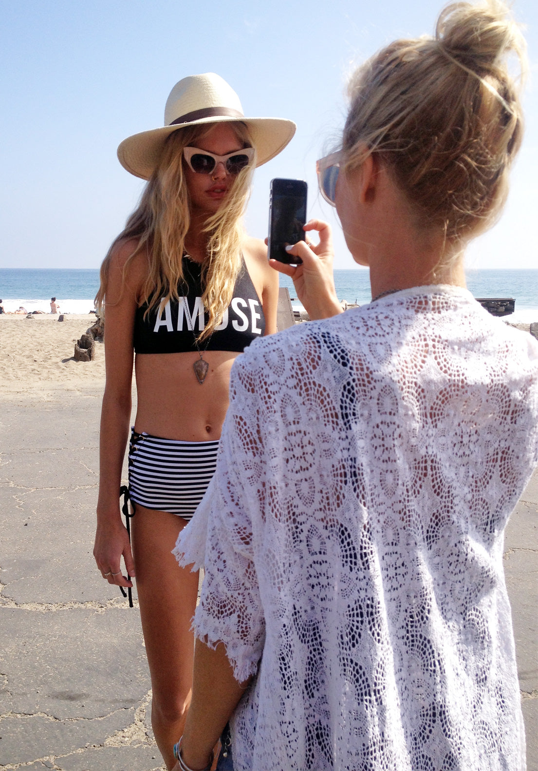 Woman taking photos of model in Amuse swimsuit on the beach